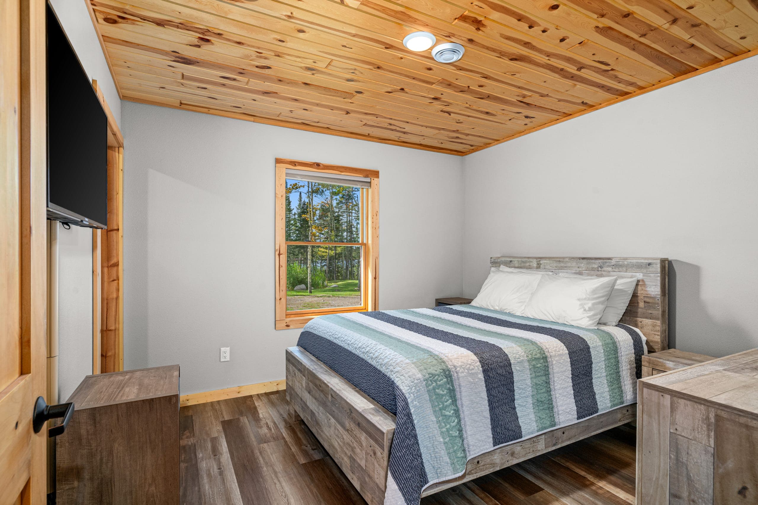 Queen bedroom with a striped quilt and a window to the trees