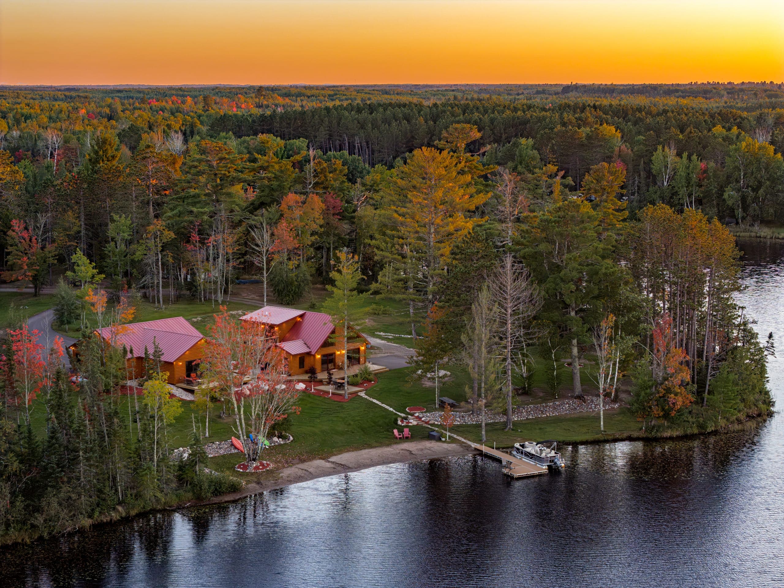 Aerial of the log cabin on a wooded point on the lake at sunset