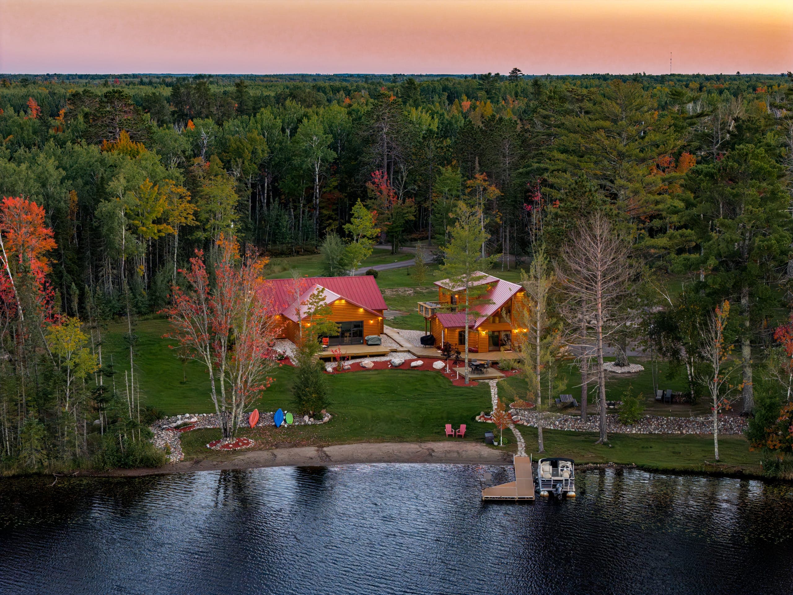 The cabins, beach, and dock from over the lake under a pink sky