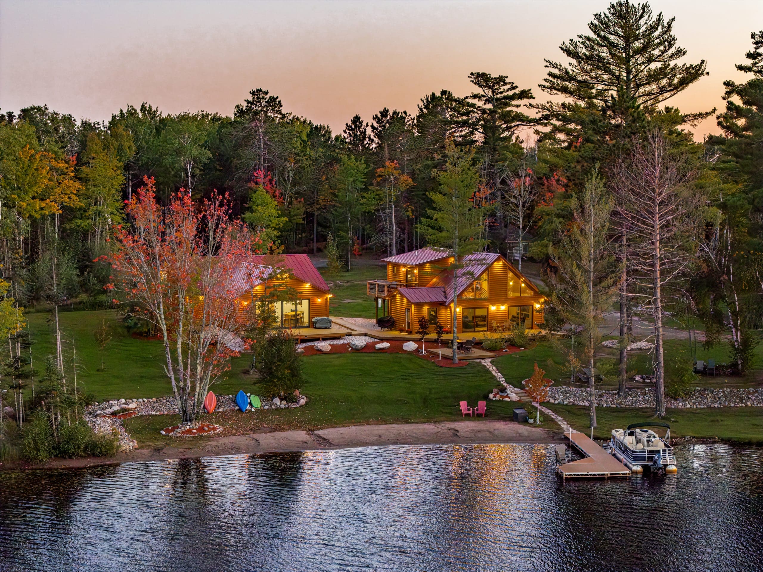 Both cabins glowing at dusk above the beach, dock, and pontoon