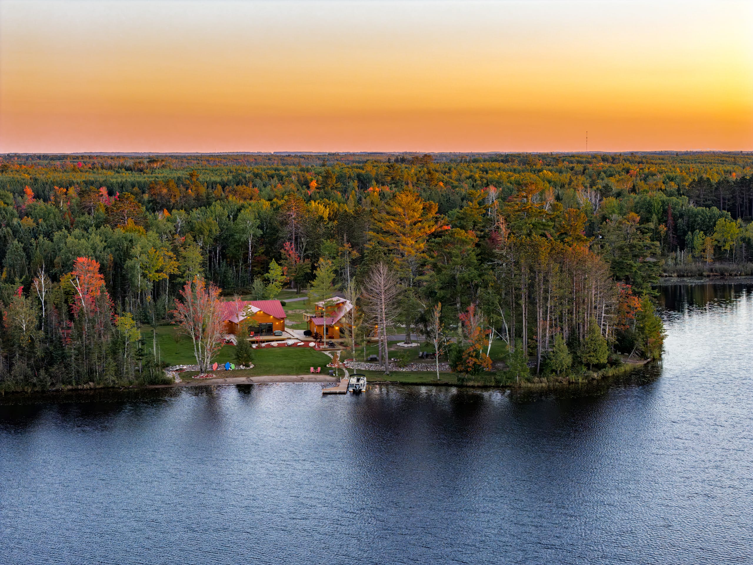 The cabins on a wooded point on the lake, under an orange sunset